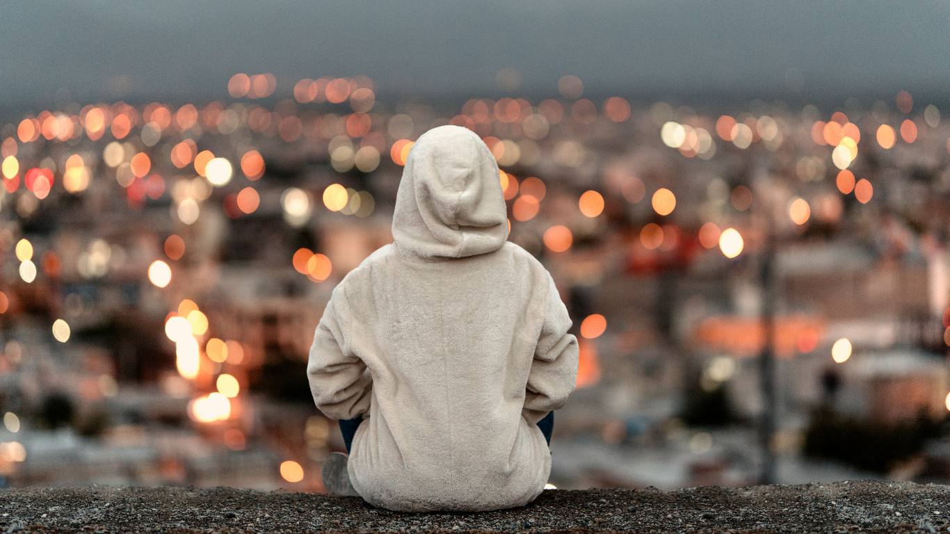 パーカー姿の女性が一人で腰かけ、ぼかした都心の景色を眺めている後ろ姿
